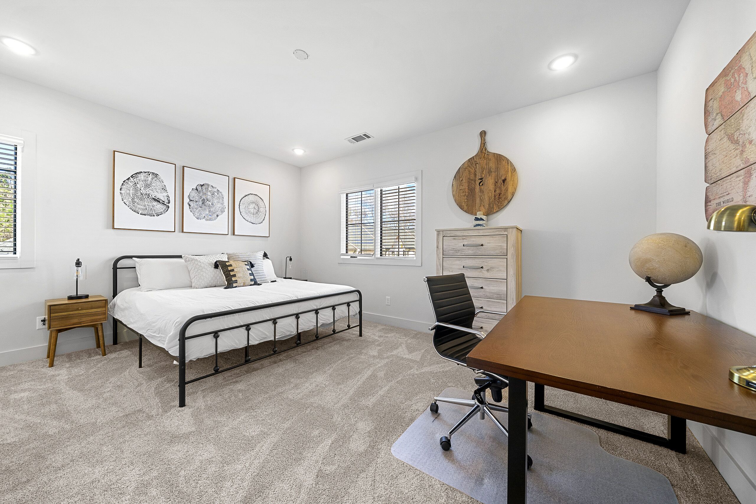 Un dormitorio con cama, escritorio, silla, cómoda y cuadros en la pared.