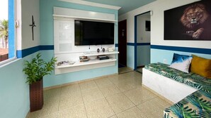 A room with a flat-screen TV mounted on a white shelf, a sofa with a tropical print, and a large framed picture of a lion on the wall. - Pousada BellMar (Cabo Frio)
