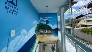 A corridor with a mural of a beach scene and a sign reading 'POUSADA BELLMAR Cabo Frio.' - Pousada BellMar (Cabo Frio)