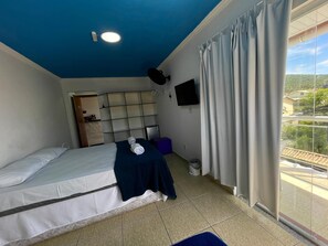 A hotel room with a bed, a flat-screen TV, a ceiling light, a window with curtains, and a view of the outside. - Pousada BellMar (Cabo Frio)