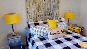A bed with a checkered bedspread, two lamps on either side, a nightstand with a lamp, and a pillow with the text "home sweet home". - Bluebird Cottage A: Across from Lake Monticello, Near Charlottesville, 1 Dog Ok (Palmyra)