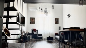 Ein modernes Wohnzimmer mit Sofa, Sessel, Esstisch und einer Treppe.