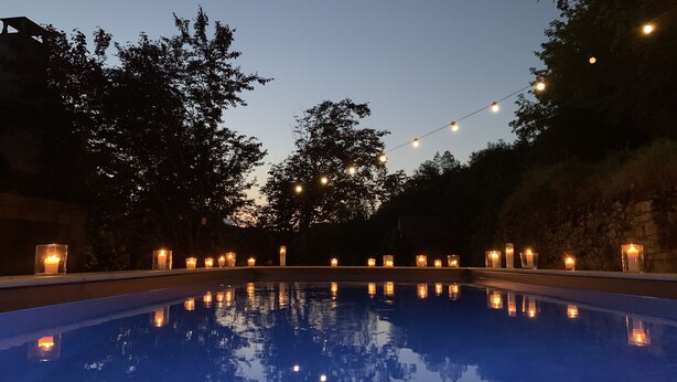 Ein Schwimmbecken im Dämmerlicht mit Lichterketten und Kerzen darum.