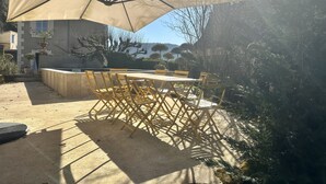Eine Terrasse im Freien mit Tisch und Stühlen, einem großen Sonnenschirm und Blick auf Bäume und Hügel.