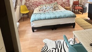 Ein Schlafzimmer mit einem Bett, einem Sessel, einem zebramusterten Sofa, einem kleinen Tisch und einer Wand mit einem Baum-Wandbild.