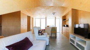 Ein modernes Wohnzimmer mit einem weißen Sofa, einem Fernseher und einem Essbereich mit Tisch und Stühlen.