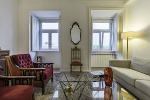 Un salon avec un fauteuil rouge, une chaise en bois, une table basse en verre et un canapé.
