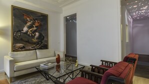 A living room with a large classical painting, a sofa, a coffee table, and a red armchair. - Chiado Prime Suites I by Homing (Lisbon)