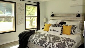 Un dormitorio con cama, ventilador de techo, ventana con persianas y aire acondicionado de pared.
