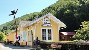 A yellow building labeled "4th Avenue Gallery Marlinton" with a wooden bench and a flag outside.