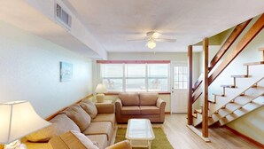 A living room with a sofa set, a coffee table, a lamp, and a staircase. - Affordable Gulf Front Triplex (Port Saint Joe)