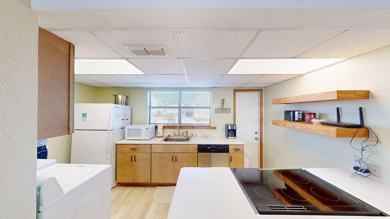 A compact kitchen with a microwave, sink, and stove. There are wooden cabinets and a window with blinds.