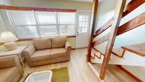 A cozy living room with a beige sofa, a small table with a lamp, and a staircase with wooden railings. - Affordable Gulf Front Triplex (Port Saint Joe)