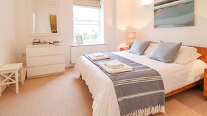A bedroom with a bed, a dresser, a nightstand, a lamp, a window, and a painting on the wall. - Feathers, Blythburgh (Halesworth)