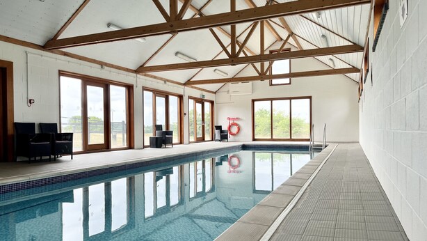 An indoor swimming pool with clear blue water, wooden beams on the ceiling, and large windows offering views of the outdoors. - Feathers, Blythburgh (Halesworth)