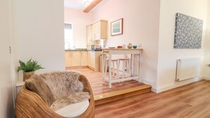 A modern kitchen with wooden cabinets, a white countertop, and a small bar area with stools. - Feathers, Blythburgh (Halesworth)