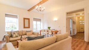 A spacious living room with a large beige sofa, a dining table set for four, and a chandelier. - Feathers, Blythburgh (Halesworth)