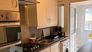 A compact kitchen with a stove, oven, and washing machine. - Budget 5-bed Apartment in Barking (Barking)