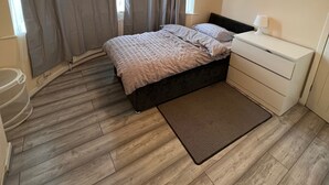 A bedroom with a bed, bedside table, and a window with curtains. - Budget 5-bed Apartment in Barking (Barking)