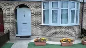 A house with a blue door, a brick facade, and a bay window with multiple panes. - Budget 5-bed Apartment in Barking (Barking)