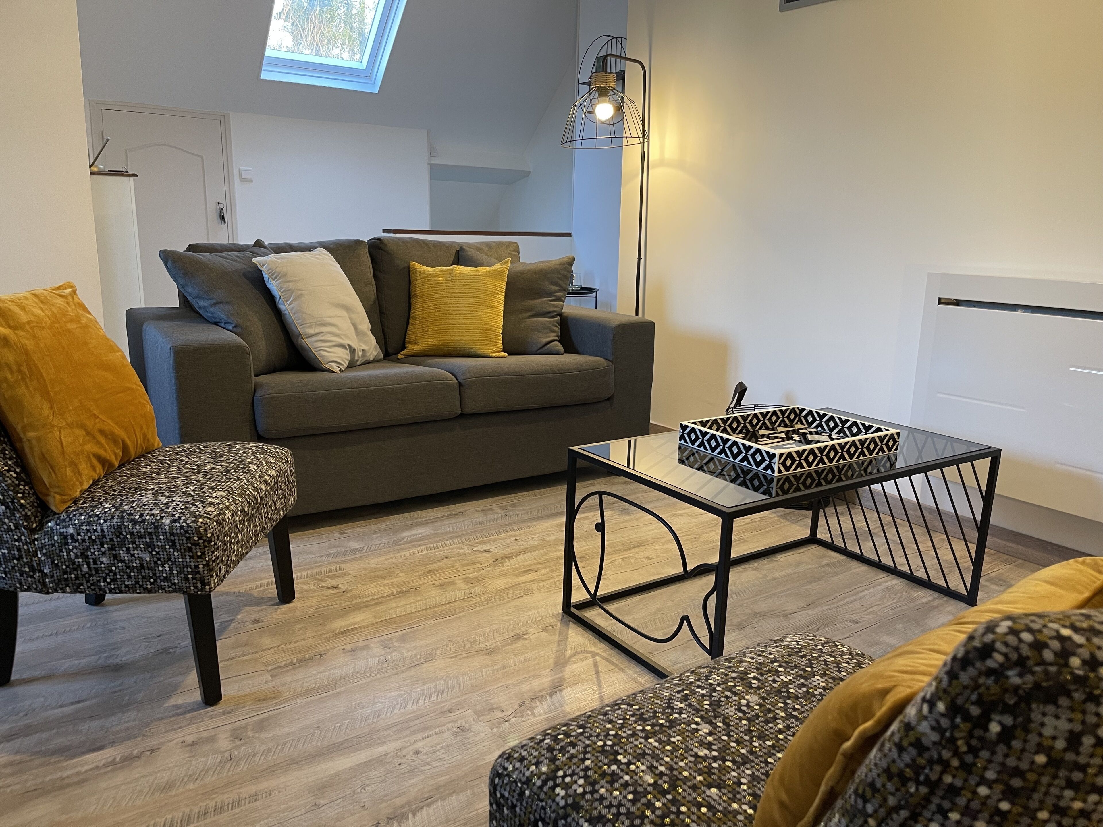 Ein modernes Wohnzimmer mit grauem Sofa, gemustertem Sessel und einem Glastisch.