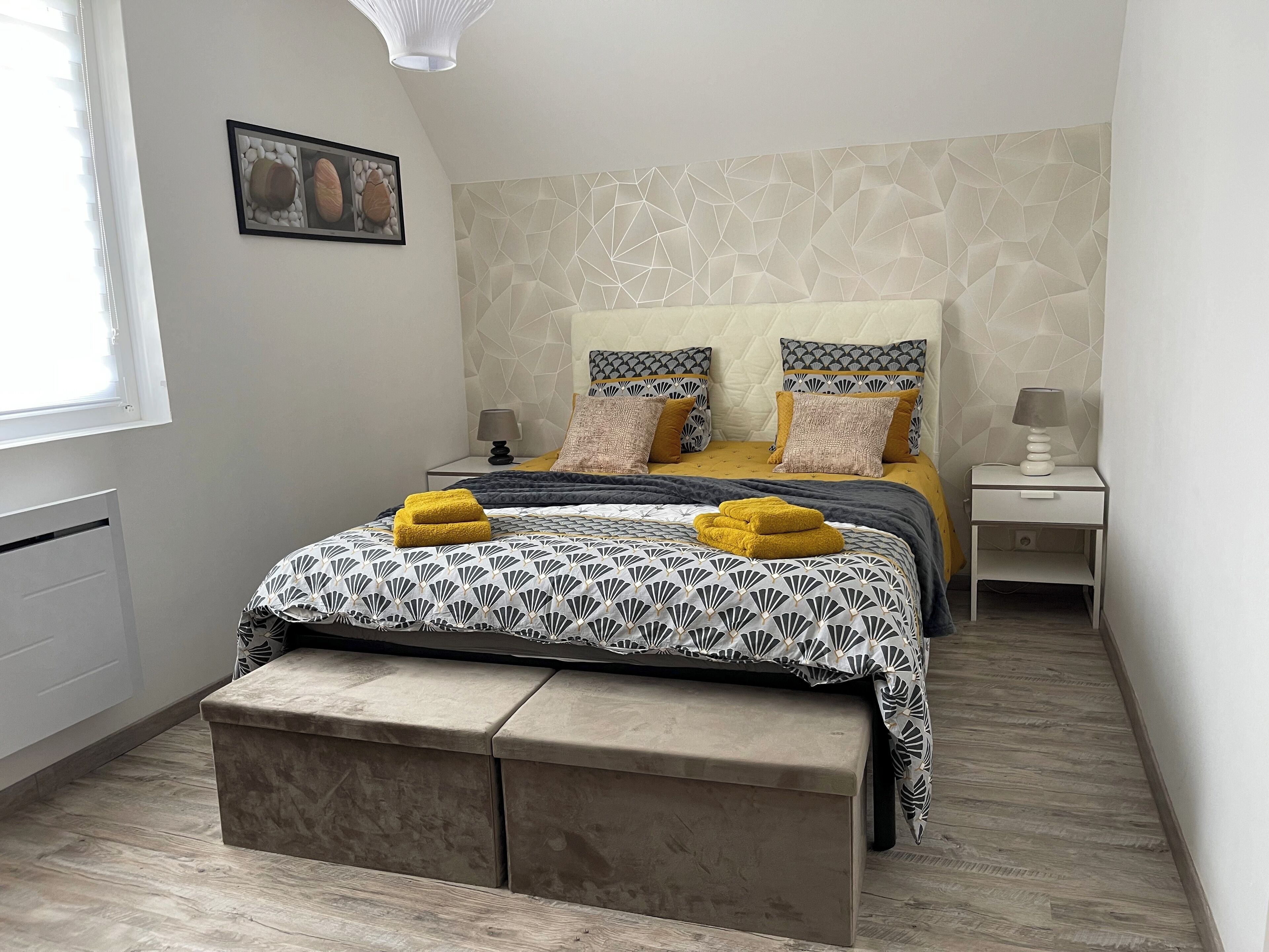 A bedroom with a bed, bedside tables, a bench, a picture on the wall, and a window.