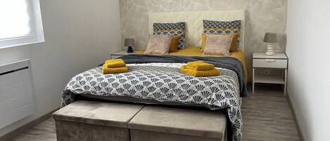 A bedroom with a bed, bedside tables, a bench, a picture on the wall, and a window.
