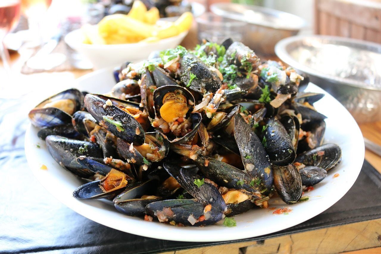 A plate of mussels garnished with herbs, served on a white plate.