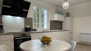 A modern kitchen with white cabinetry, a round dining table, and a bowl of fruit. - COTE D'ALBÂTRE BEACH 5 MINUTES AWAY (Criel-sur-Mer)