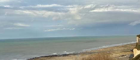 A coastal landscape with a sandy beach, rocky cliffs, and a cloudy sky.