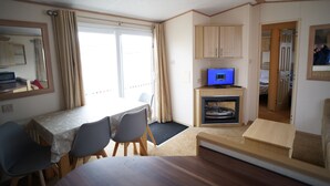 Une pièce de taille modeste comprenant une table à manger, des chaises, un téléviseur, une cheminée et un miroir.