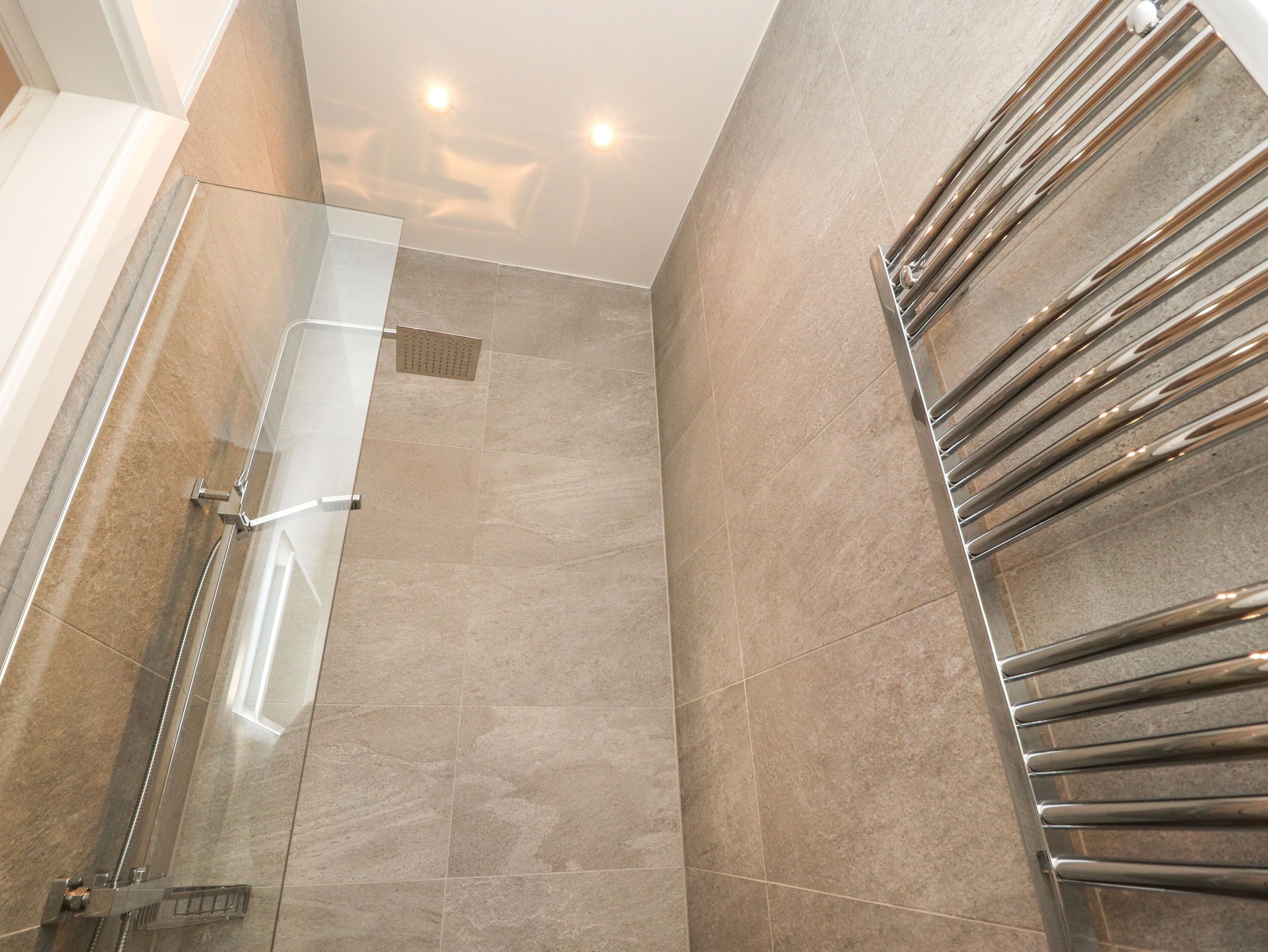A modern bathroom with a glass shower enclosure, a stainless steel towel rack, and beige tiled walls.