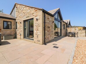 A stone building with a glass door entrance, outdoor seating area, and a stone wall. - Ribble View (Clitheroe)