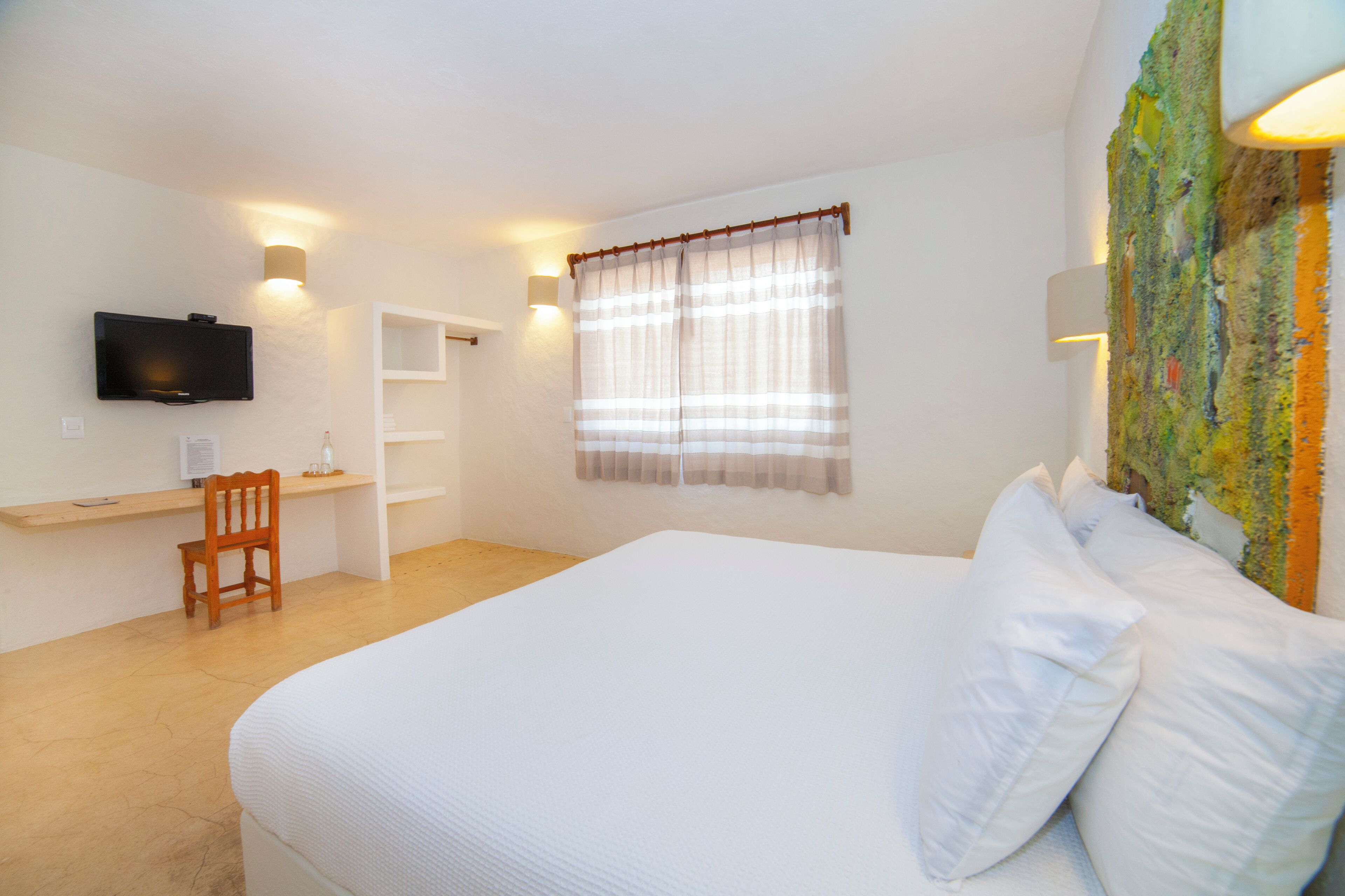 A bedroom with a large bed, a desk, a chair, a television, and a window with curtains.