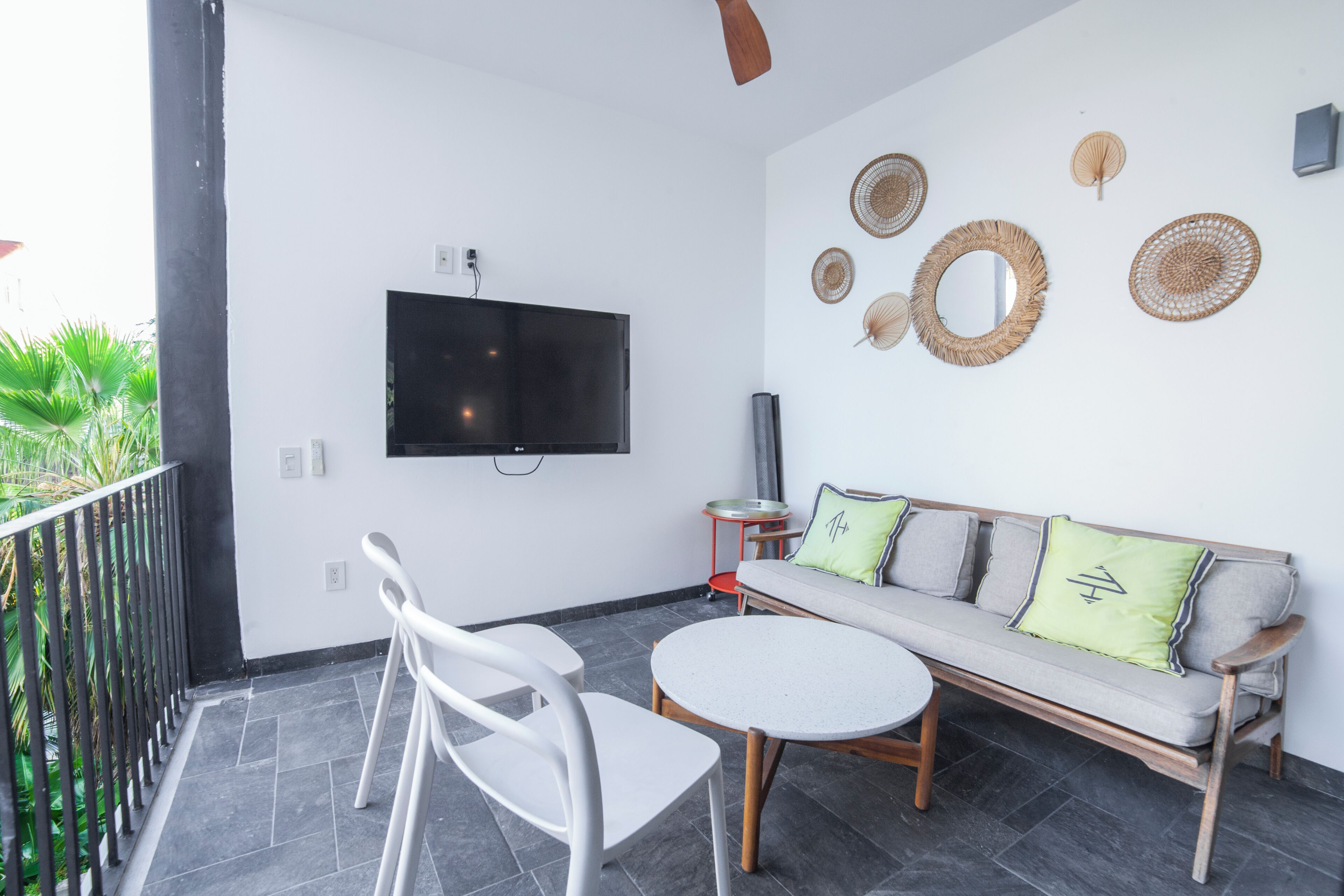 A balcony with a sofa, two chairs, a round table, and a flat-screen TV mounted on the wall.