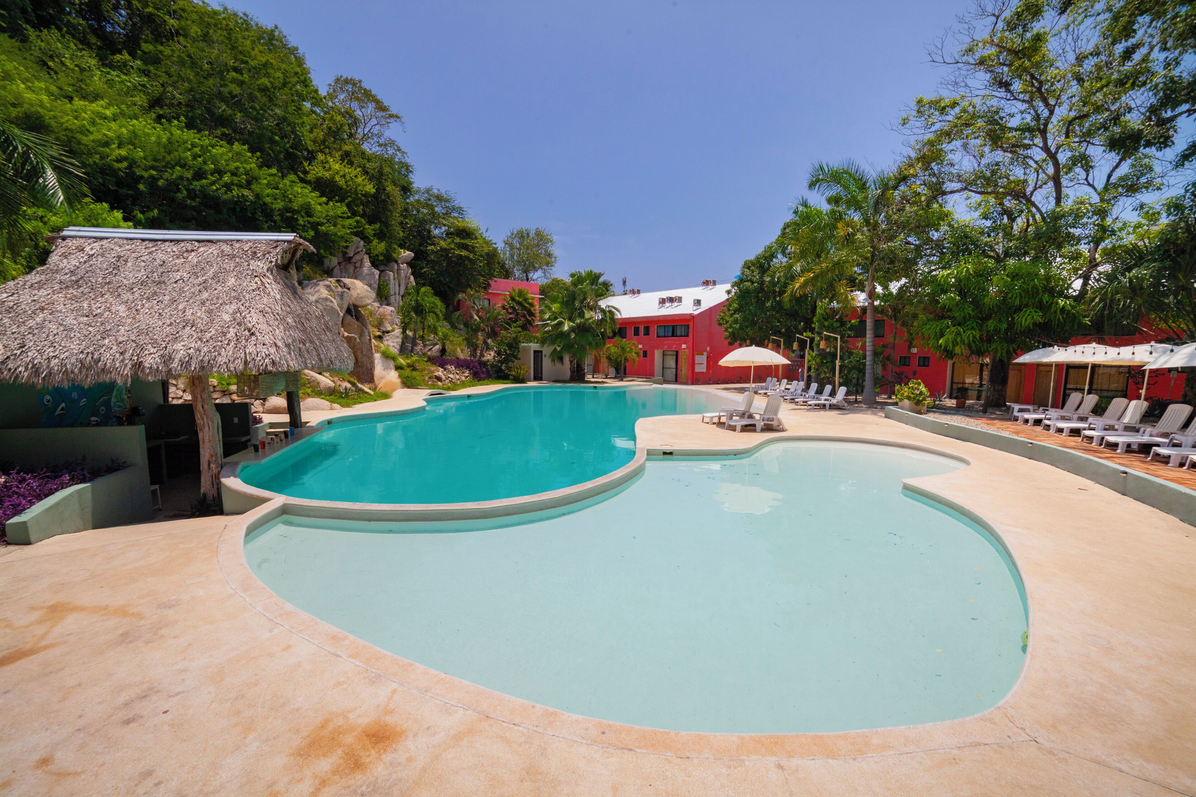 Una piscina de disseny corbat, envoltada de gandules i una estructura de palla.