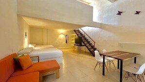 Un amplio espacio de sala con sofá, mesa de comedor, televisor y una escalera que sube a un nivel superior.