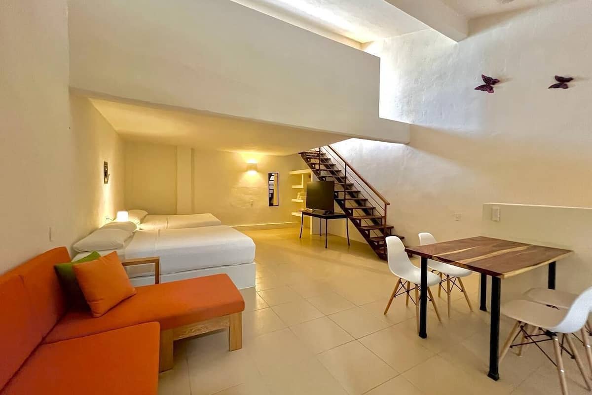 A spacious living area with a sofa, a dining table, a TV, and a staircase leading to an upper level.