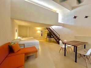 Un'ampia zona giorno con divano, tavolo da pranzo, televisore e una scala che conduce al piano superiore.