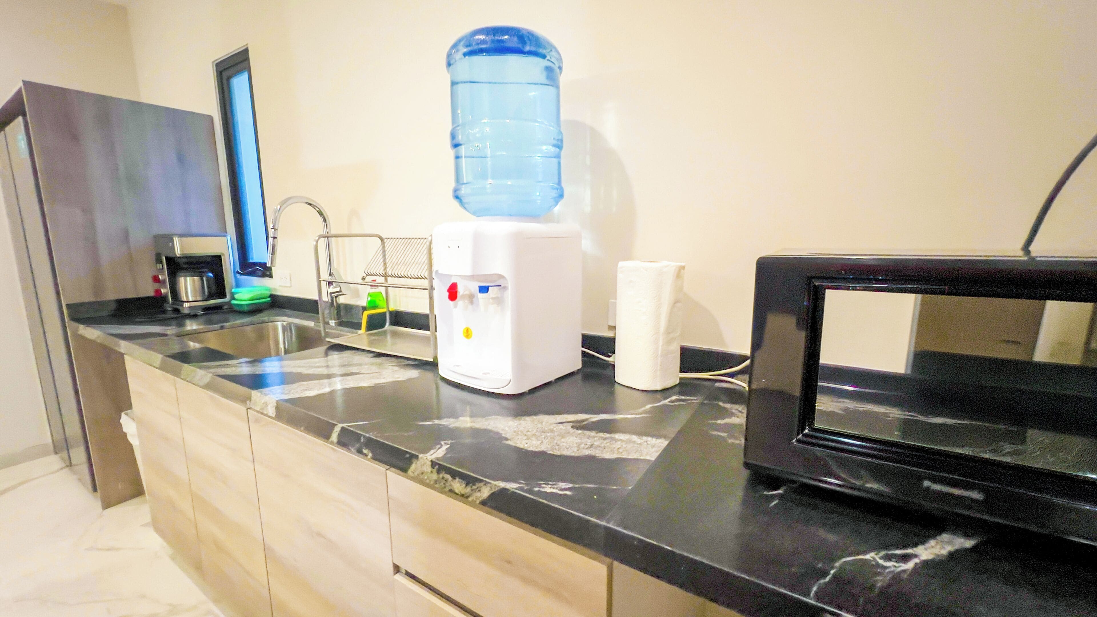 Una cocina con dispensador de agua, cafetera, microondas y televisor.