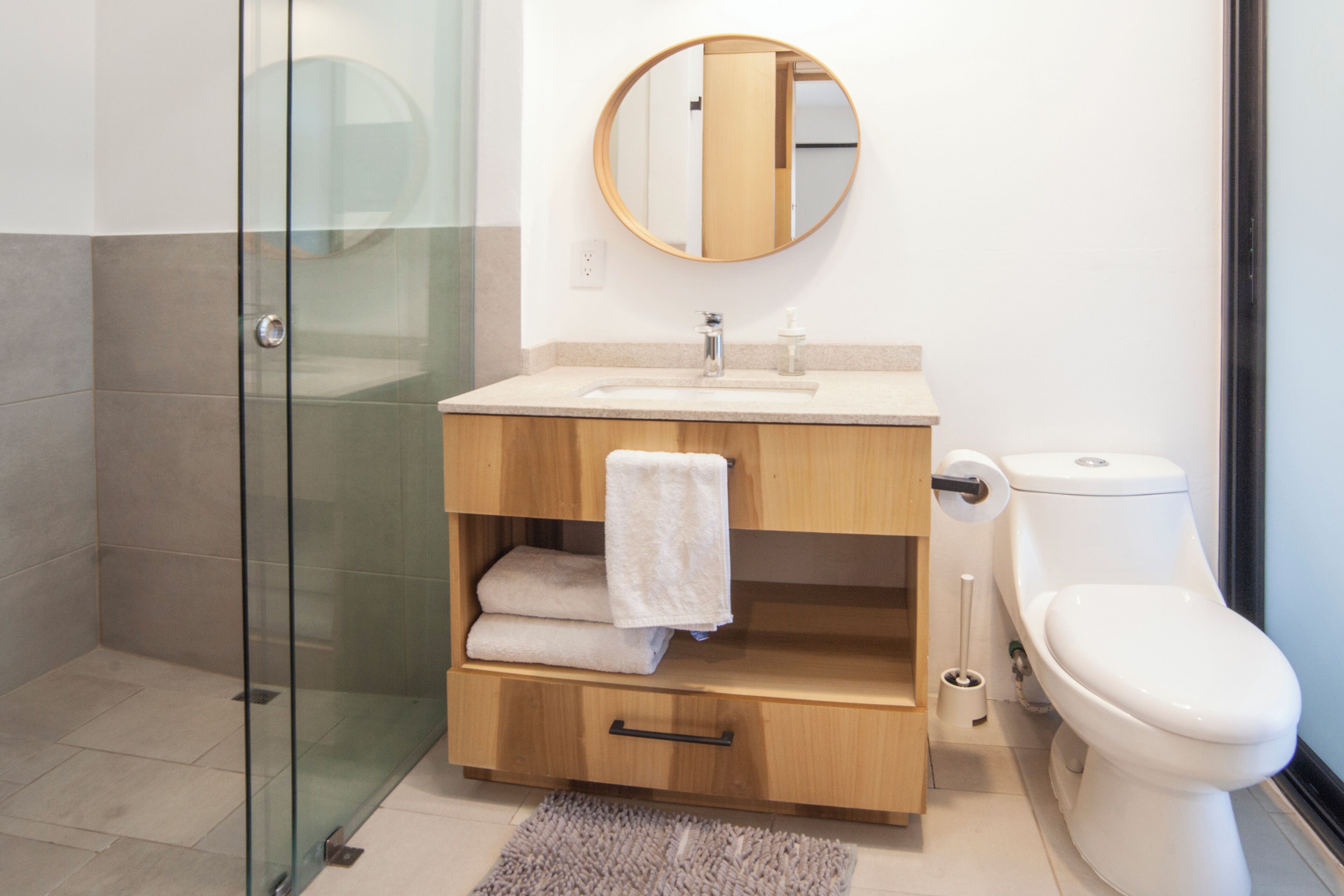 Un baño moderno con cabina de ducha de vidrio, tocador de madera con lavamanos, inodoro y espejo sobre el tocador.
