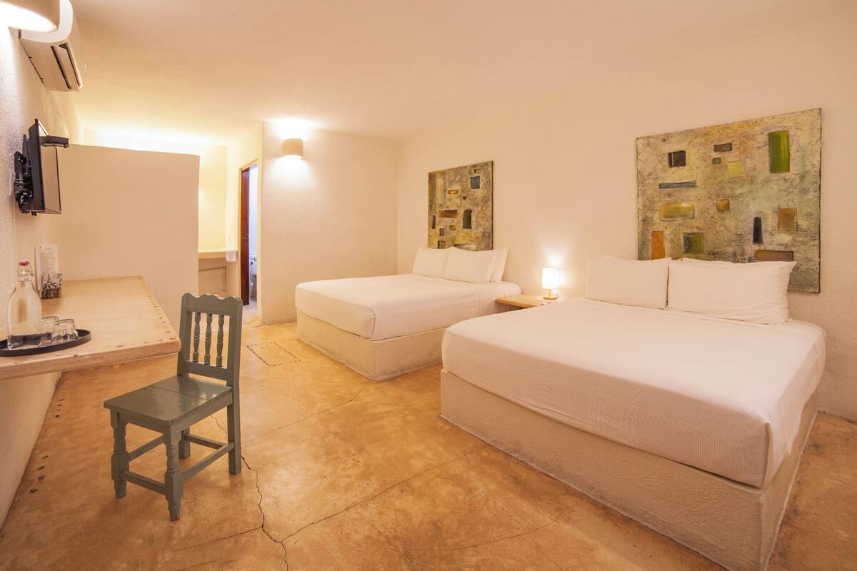 A hotel room with two beds, a chair, a desk, and artwork on the walls.