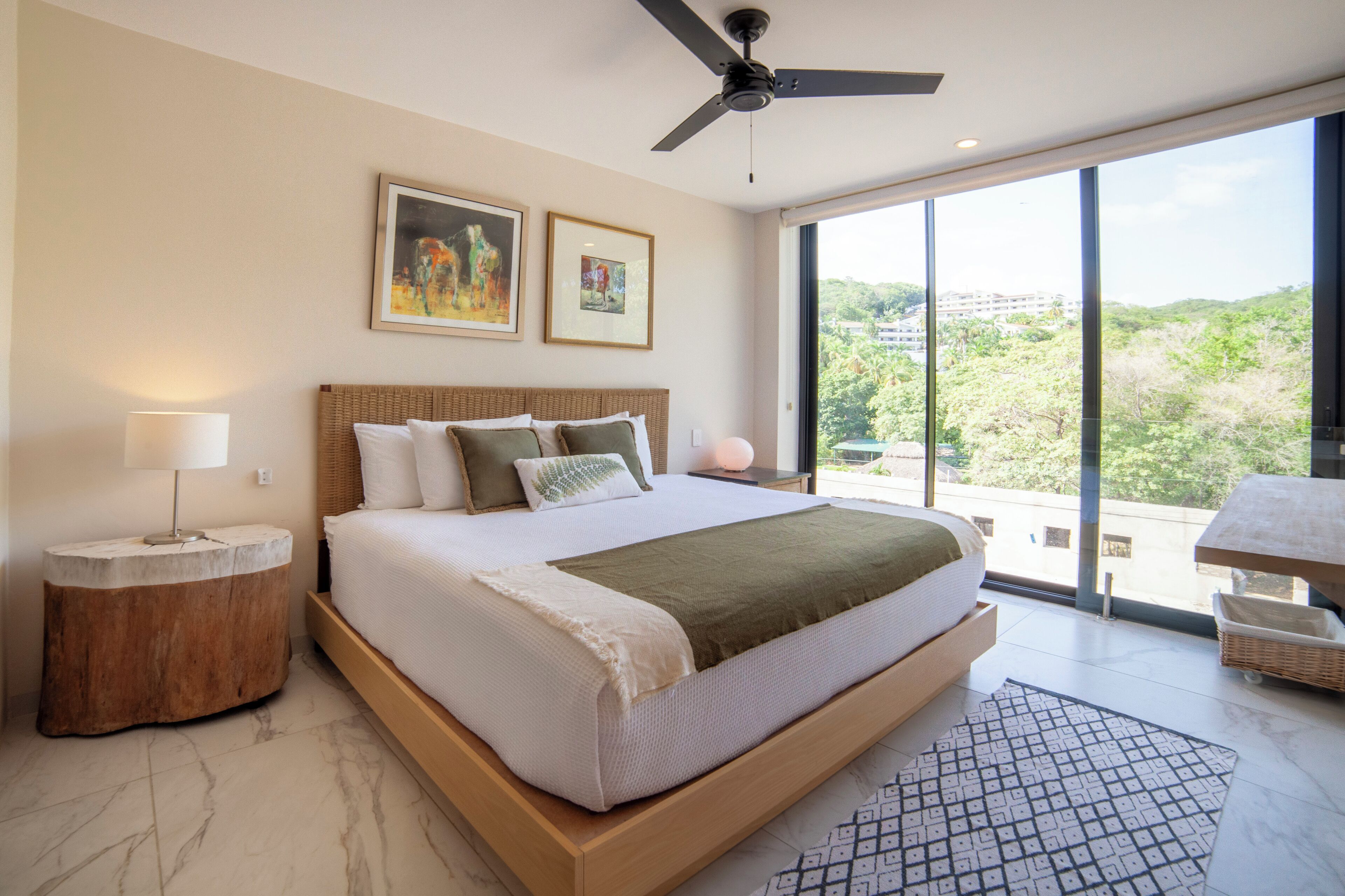 Un dormitorio moderno con una cama grande, ventilador de techo y vistas al exterior.