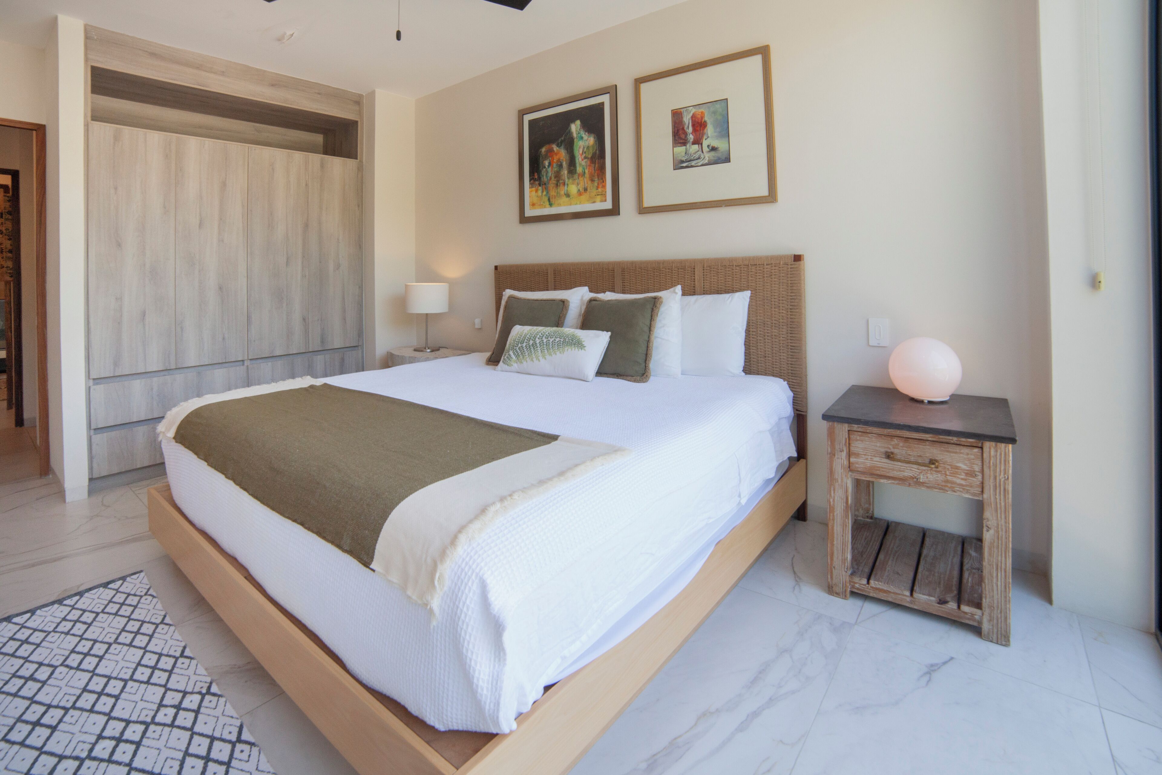 A modern bedroom with a large bed, a wooden headboard, a bedside table, and a wall-mounted wardrobe.
