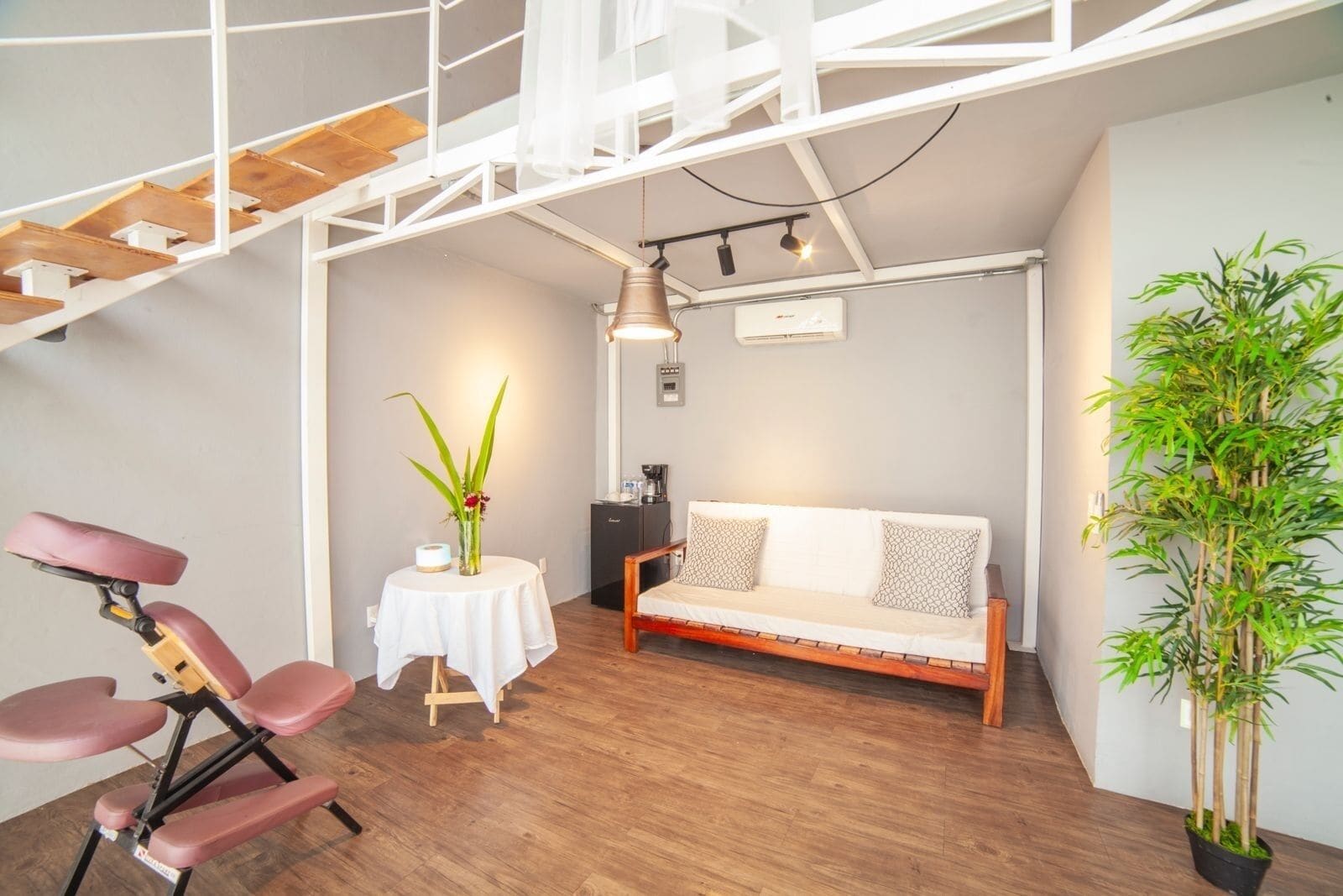 Et moderne værelse med en sofa, et lille bord med en vase, en stol, en trappe og en potteplante.