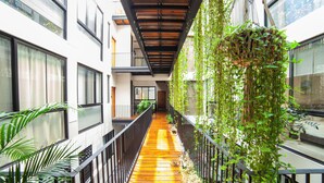 Un pasillo con suelo de madera, barandillas metálicas y plantas verdes en las paredes.