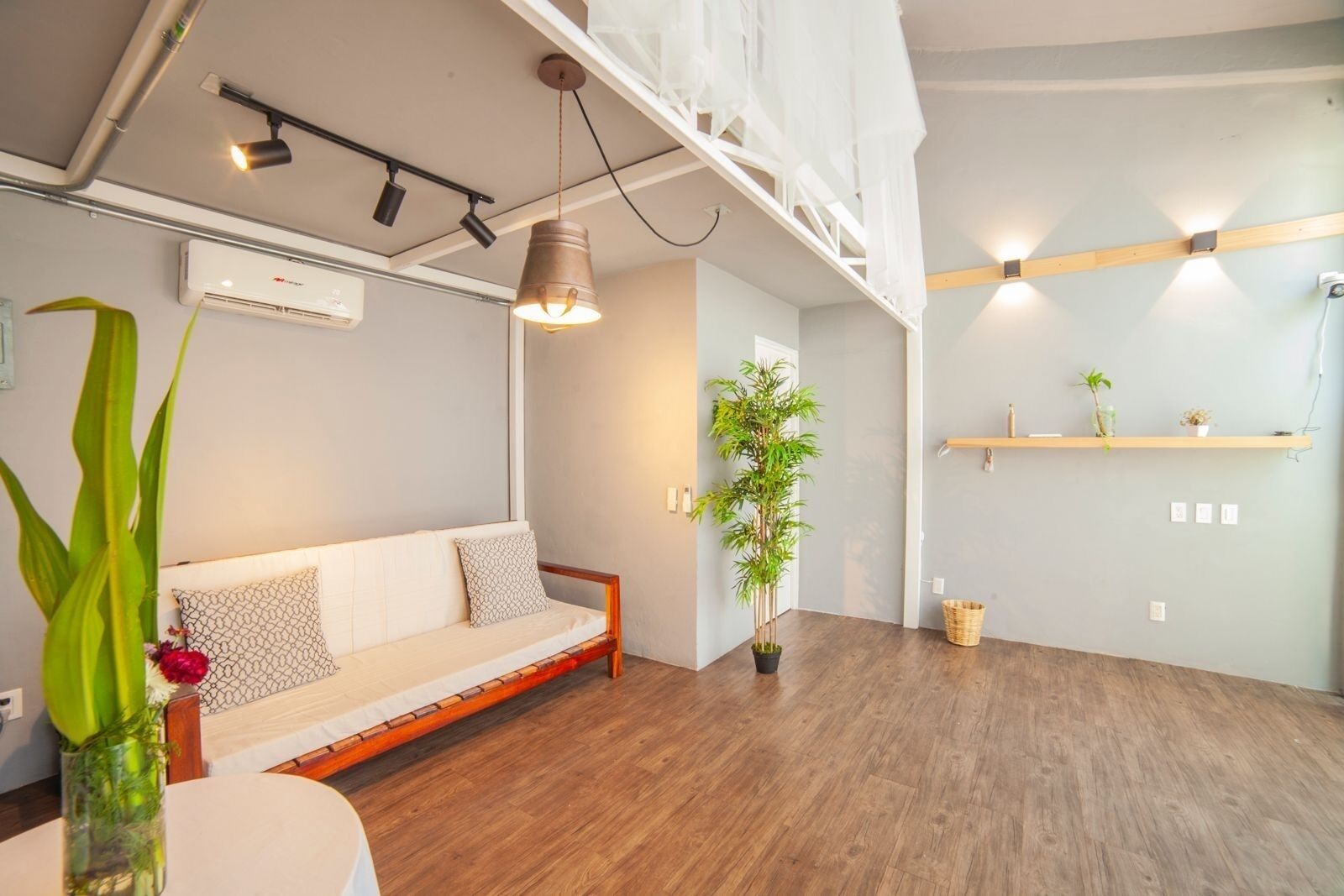 A modern living room with a wooden floor, a white sofa, a hanging light fixture, and a potted plant.