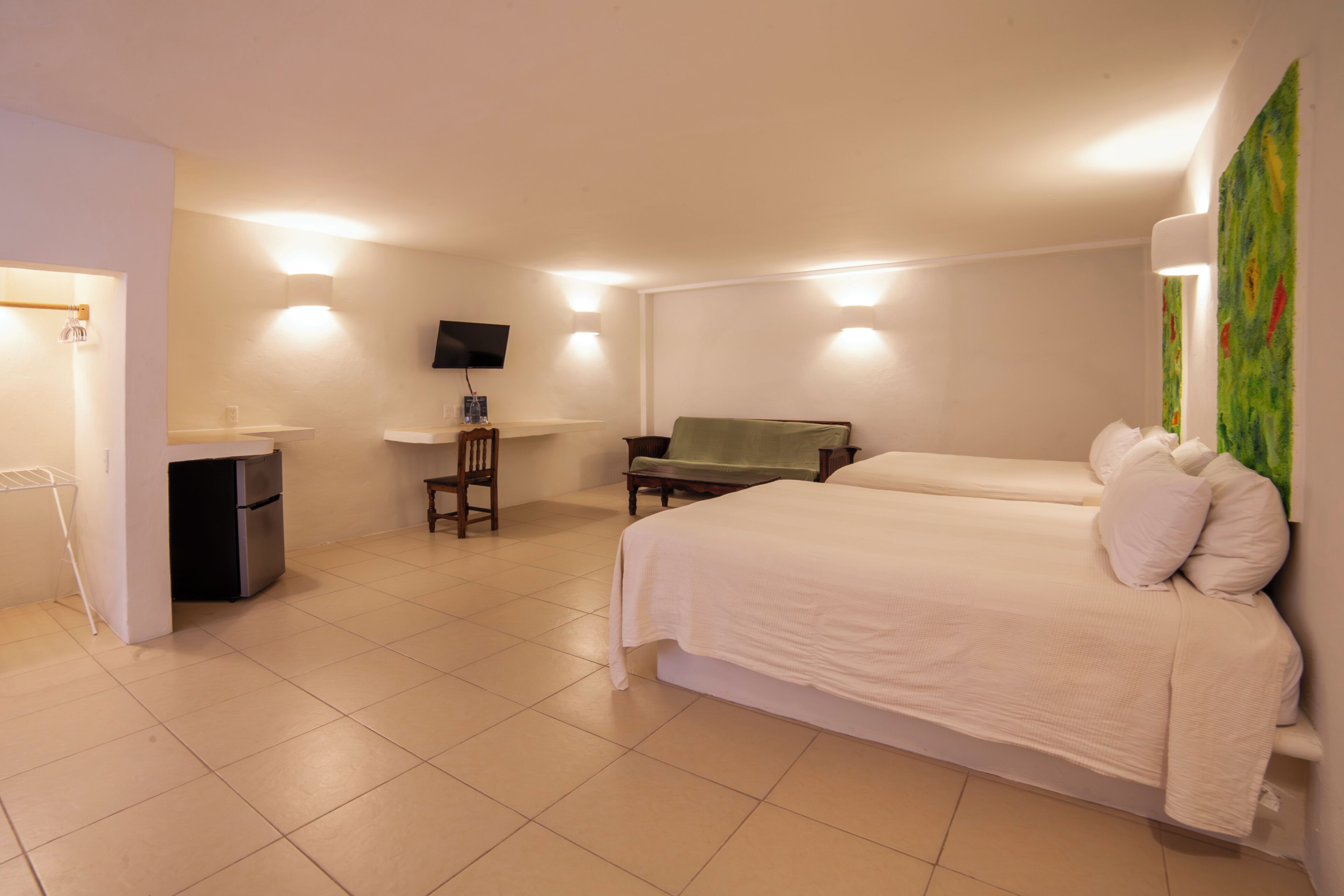 A hotel room with a bed, a desk, a chair, a TV, and a painting on the wall.