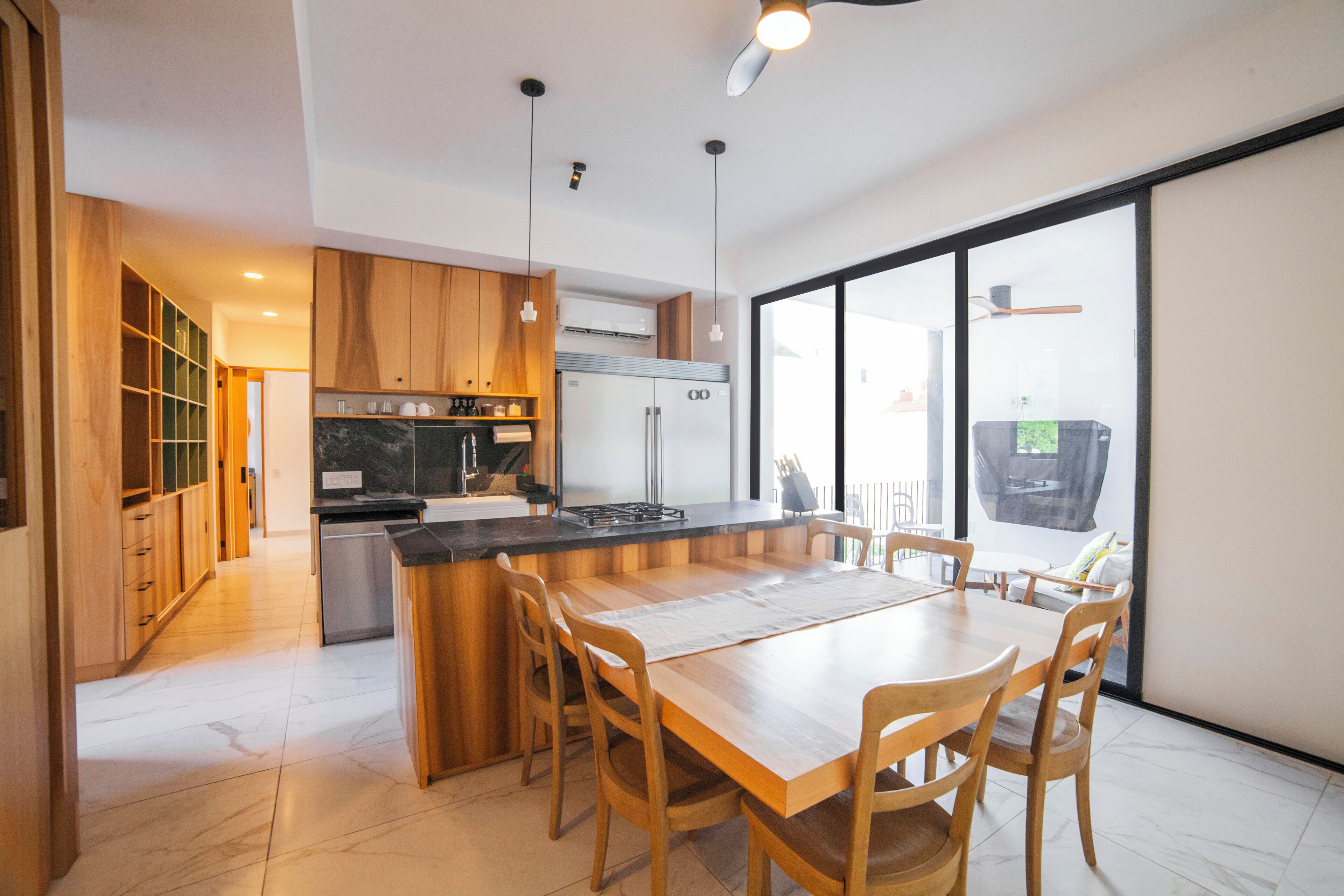 A modern kitchen with wooden cabinets, a central island with seating, and a large window providing a view of the outdoors.