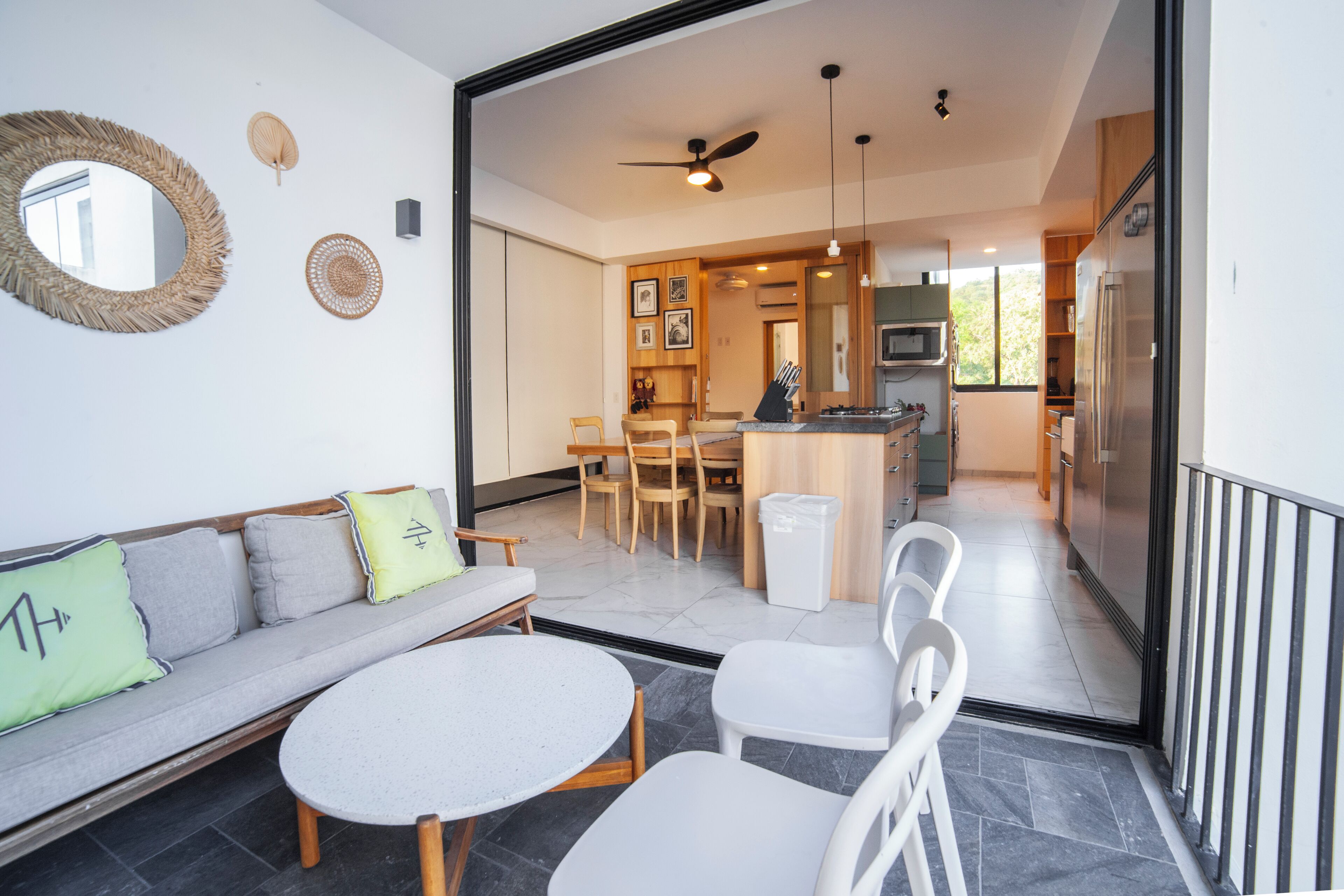 Una sala moderna con un sofá, sillas y una mesa de comedor. Se ve una cocina al fondo, con un refrigerador y armarios.